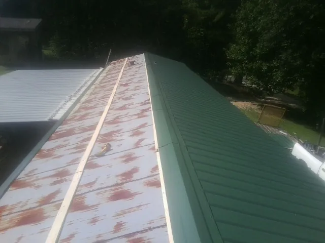 Old rusted panels beside newly installed green metal roofing — Wind Damage Roof Repair by Roofing Brothers in Clarence