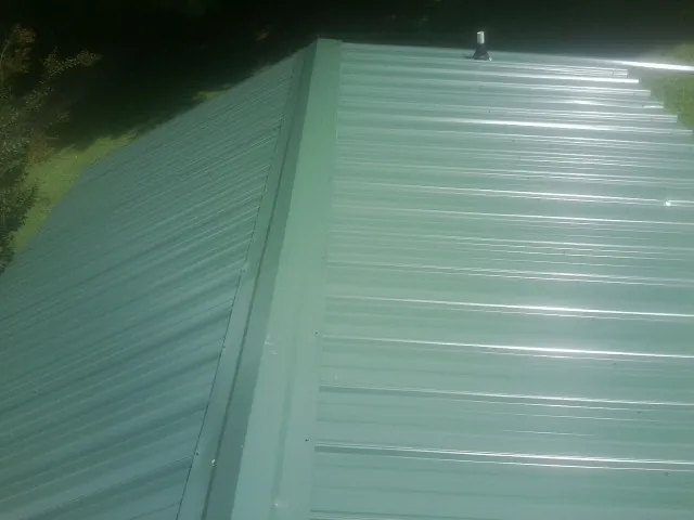 New green metal panels meeting at the ridge of a roof — Flat Roof Repair work by our crew in Clarence