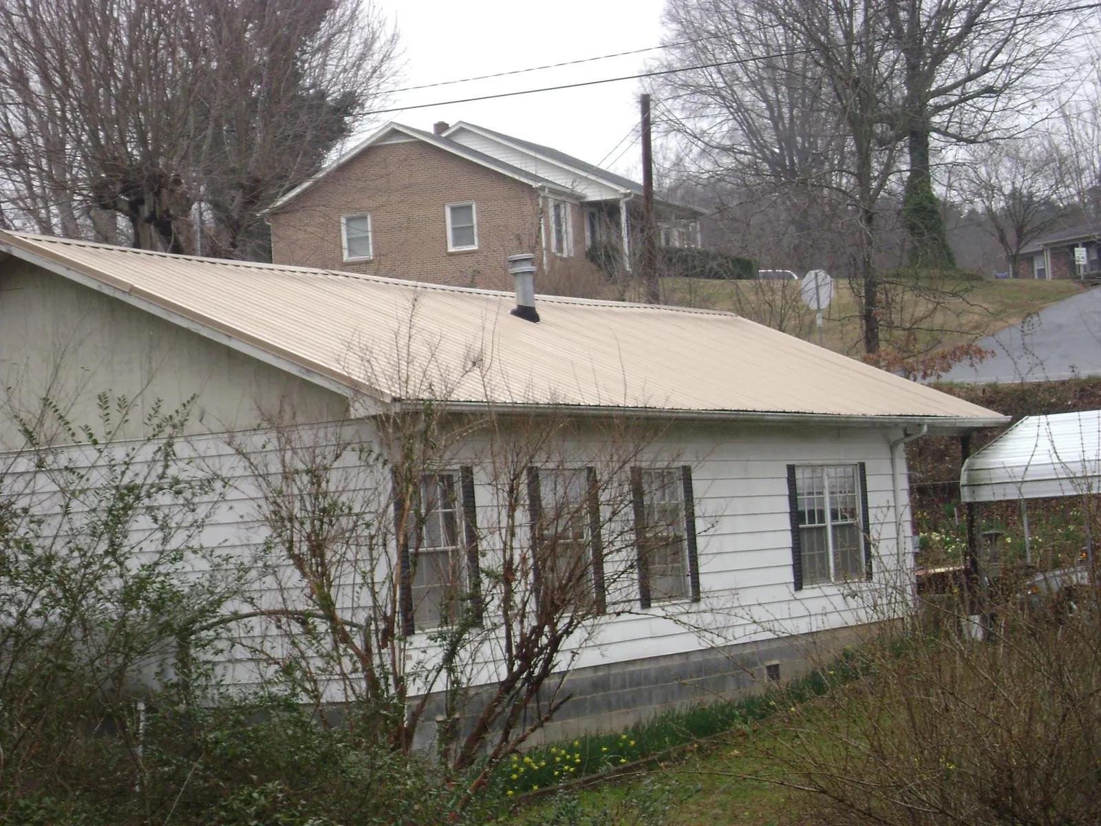 Tan metal roof on a white sided house set into a hillside — Commercial Roofing by Roofing Brothers in Clarence